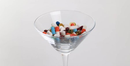 Foto de Vidrio con muchas cápsulas médicas multicolores en primer plano de fondo blanco. Concepto de polifarmacia - Imagen libre de derechos