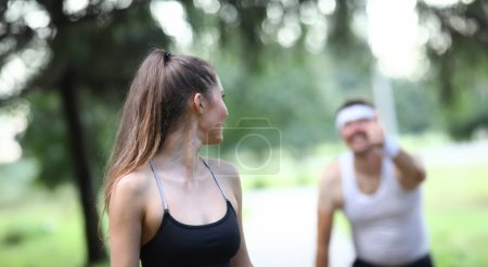 Slender girl looks back at man showing ok gesture. Adherents healthy lifestyle are running around park. People have found way to recharge their day with positive energy. Guy compliments girl.