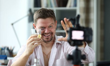 Drunk male director holds a glass with whiskey in hand and greets his subservient portrait. Work of dream concept