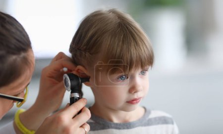 Otorhinolaryngologist examines little girls ear with otoscope. Adenoiditis as cause of otitis media in children concept.