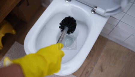 Gloved hand is cleaning toilet with brush. Home cleaning services concept