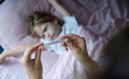 Woman hand holding mercury thermometer with high temperature against background of sick girl closeup. Seasonal colds in children concept