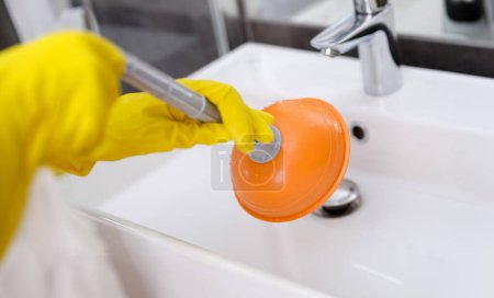 Foto de Fontanero con guantes de goma fregadero de limpieza con émbolo en primer plano baño. Marido por concepto de hora - Imagen libre de derechos