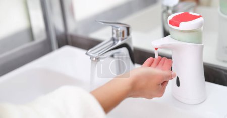 Frau holt Flüssigseife aus Handspender in Badezimmer-Nahaufnahme. Konzept moderner Hygienetechnologien