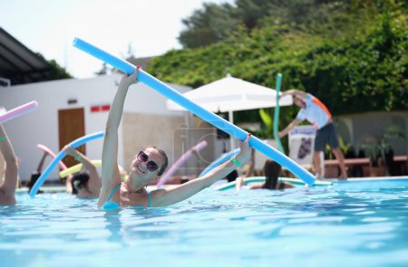 Téléchargez les photos : Femme attrayante faisant des exercices avec des nouilles est engagée dans l'aquagym. Avantages de l'exercice sportif dans le concept de l'eau - en image libre de droit