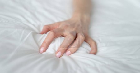 Téléchargez les photos : Woman hand tightly grips white sheet on bed. Nightmares and temper tantrums in the morning - en image libre de droit