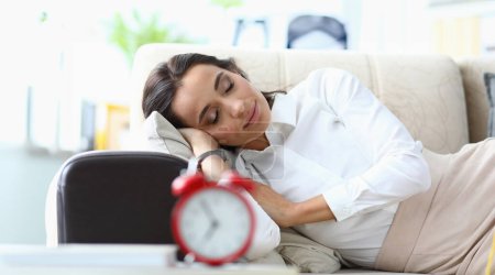 Junge Frau schläft auf Sofa neben Wecker. Müdigkeit und Schläfrigkeit bei Frauen