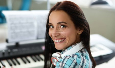 Primer plano de sonriente maravillosa mujer tocando sintetizador en notas. Hermosa chica con auriculares inteligentes de moda. Concepto de música artística. Fondo borroso
