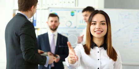 Portrait of pretty lady reaching tender arm to perform friendly gesture towards colleague or business manager. Beautiful female in classy bluse smiling at camera with joy. Company meeting concept