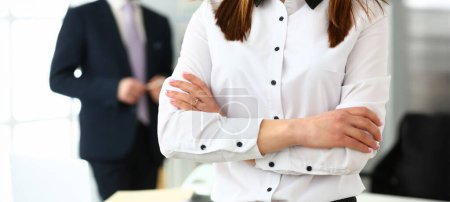 Close-up of gorgeous female standing in big modern office with crossed hands. Pretty woman discussing questionable subject with witty colleagues and managers. Company meeting concept