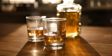 Im Mittelpunkt stehen zwei Glasflaschen mit Whiskey oder Bourbon auf einem Holztisch. Luxusgetränk mit Eiswürfeln auf dem Tisch. Festkonzept. verschwommener Hintergrund