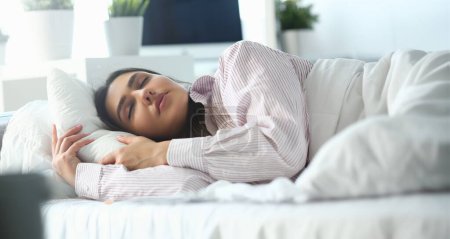 Beautiful indian woman peacefully lying in bed sleeping early morning while alarm clock going to ring awakening. Early wake up, not getting enough sleep, oversleep, getting work time concept