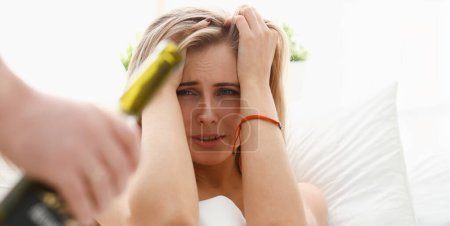 Photo for The drinking man brings bottle of wine to girlfriend in the morning who has hangover and has strong headache. They had sex on drunk intoxicated, which the girl very much regrets - Royalty Free Image