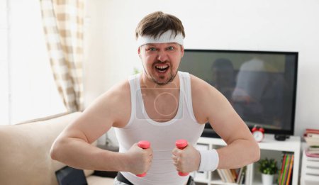 Photo for Young attractive man engaged in fitness at home holding dumbbell in hand trying to fight excess weight and loss - Royalty Free Image