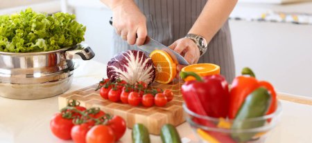 Photo for Chef Chop Juicy Orange Fruit Kitchen Photography. Vegan Cut Citrus with Knife in Hands. Healthy Vegetable Ingredient for Salad. Fresh Tomatoes, Cabbage and Pepper in Bowl. Culinary Blog Closeup Shot - Royalty Free Image