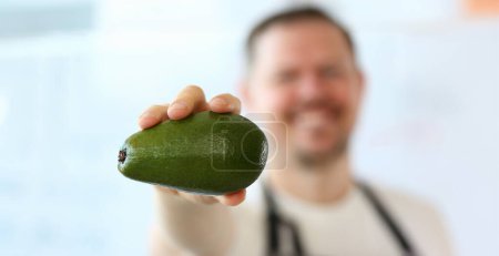 Photo for Chef Showing Exotic Green Avocado Photography. Man Holding Ripe Tropical Fruit in Hand. Delicious and Organic Vegetarian Kitchen. Fresh and Healthy Food for Vegan. Fresh Ingredient Partial View Shot - Royalty Free Image