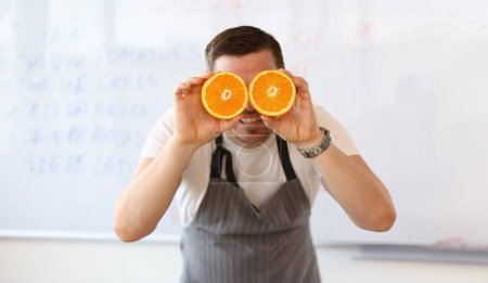 Photo for Vegan Chef Blogger Holding Cut Juicy Orange Fruit. Man with Colorful Citrus Halves on Eye in Kitchen on White Background. Concept of Healthy Food and Lifestyle. Smiling Person with Citrus in Hands - Royalty Free Image