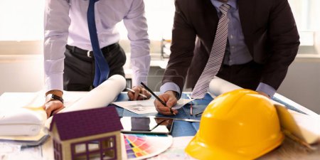 Photo for Engineer or Architectural Project Partnership. Building Design Concept. Engineering Hand Holding Pencil Making House Sketch on Blueprint. Yellow Helmet Architect Equipment at Workplace - Royalty Free Image
