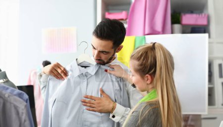 Photo for Assistant Buyer Fashion Dressmaker Sewer Service. Caucasian Stylist Standing near Male Purchaser Fitting on Formal Shirt. Girl Designer Consulting about Outfit. Couple at Dressmaking Atelier - Royalty Free Image