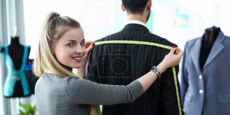 Photo for Classy Clothes Design Tailor Craftsmanship Concept. Female Sewer Standing near Male Client Measuring Shoulder Width. Beautiful Woman Taking Measures for Business Suit Using Tape Meter - Royalty Free Image