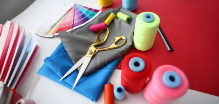 Photo for Fashion Designing Tailor Craftsmanship Concept. Fabric, Color Palette and Sewing Tools on Table. Needle Machine Bobbins Spools of Thread with Gold Scissors on Silk Piece. Designer Working Desk - Royalty Free Image