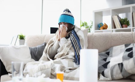 Photo for Portrait of woman having severe flu at home indoors and sneezing into tissue. Girl sitting in living room covered in blanket and suffering from common and annoying cold. Hard virus concept - Royalty Free Image