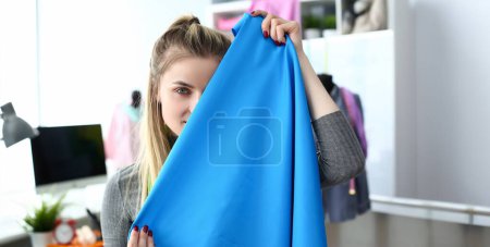 Photo for Fashion Clothes Design Fabric Selection Concept. Young Woman Dressmaker Holding Material Sample infront of Face. Caucasian Beautiful Designer Present Textile Piece at Tailor Workshop - Royalty Free Image