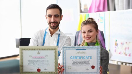 Photo for Professional Sewing Dressmaking Teamwork Concept. Happy Certified Tailors, Fashion Industry Workers Looking at Camera. Male Designer and Female Seamstress Showing Education Sertificate Document - Royalty Free Image