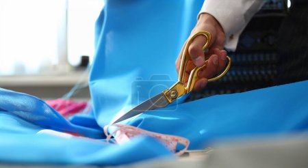 Photo for Tailoring Service Dressmaking Process Closeup Shot. Designer Hands Cutting Blue Silky Fabric Using Scissors or Shears. Textile or Fine Cloth Preparing. Sewing Tools on Dressmaker Working Table - Royalty Free Image