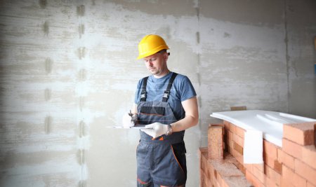 Photo for Male builder in yellow hard hat holds clipboard on background of an apartment under repair portrait. Estimated property value concept. - Royalty Free Image