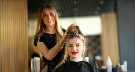 Photo for Girl Client Getting Hairstyle by Hairdresser. Hairstylist Holding Hair of Female Customer for Styling New Haircut. Young Beautician Styling Hairdo for Woman with Red Lips Looking at Camera Shot - Royalty Free Image