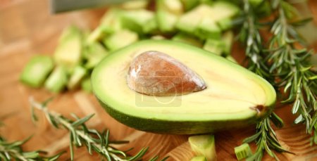 Photo for Tropical Avocado Fruit Half Holding Brown Seed. Exotic Ingredient on Wooden Cutting Board. Dieting and Healthy Food with Rosemary Herb. Tasty Appetizer. Partial View Horizontal Photography - Royalty Free Image