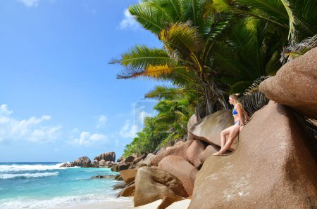 Téléchargez les photos : Femme debout sur le gros rocher de granit. Plage d'Anse Cocos à La Digue, Seychelles. - en image libre de droit