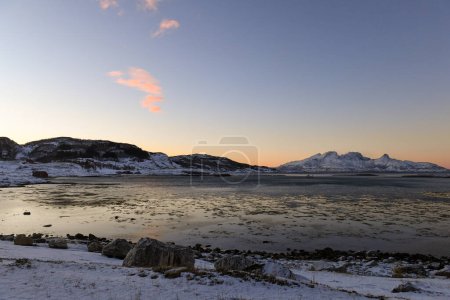 Foto de Landscape shot highlighting the rugged mountains and snow-covered beaches of arctic norway during a brief golden hour during the long winters. - Imagen libre de derechos