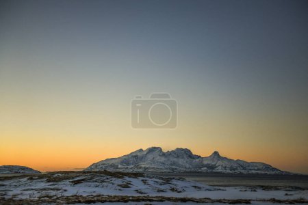 Téléchargez les photos : Landscape shot highlighting the rugged mountains and snow-covered beaches of arctic norway during a brief golden hour during the long winters. - en image libre de droit