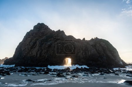 Photo for Wide-angle shot of the keyhole arch at Pfeiffer beach, California, whit the setting sun peeping through the central hole. Sunset on a winter evening in California. - Royalty Free Image