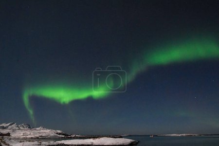 Foto de Bright Green Colours of the Northern Light, Aurora Borealis illuminate the Night Sky over the beach at Mjelle, in Arctic Norway. - Imagen libre de derechos