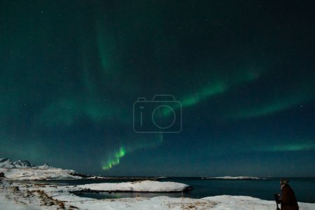 Foto de Brillantes colores verdes de la luz del norte, Aurora Borealis ilumina el cielo nocturno sobre la playa de Mjelle, en el Ártico de Noruega. - Imagen libre de derechos