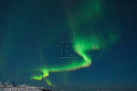 Foto de Brillantes colores verdes de la luz del norte, Aurora Borealis ilumina el cielo nocturno sobre la playa de Mjelle, en el Ártico de Noruega. - Imagen libre de derechos
