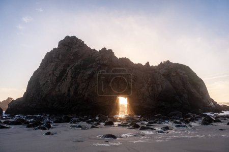 Photo for Wide-angle shot of the keyhole arch at Pfeiffer beach, California, whit the setting sun peeping through the central hole. Sunset on a winter evening in California. - Royalty Free Image