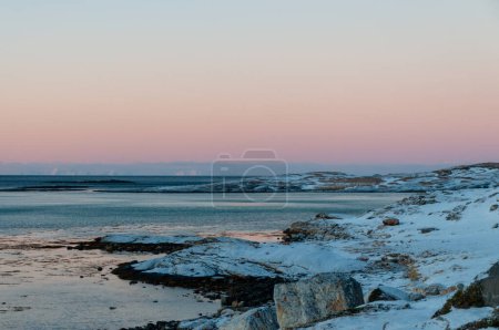 Landscape shot highlighting the rugged mountains and snow-covered beaches of arctic norway during a brief golden hour during the long winters.
