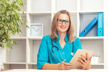 Téléchargez les photos : Jeune femme médecin en manteau turquoise dans un cabinet clinique. Concept de soins de santé. - en image libre de droit
