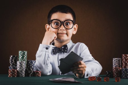 Téléchargez les photos : Un gamin jouant au poker dans un casino. Concept studio sur fond bleu - en image libre de droit