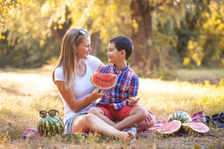 Photo for Happy smiling kid with mom eating ripe watermelon in summer park - Royalty Free Image