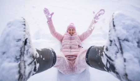 Téléchargez les photos : High angle view of happy woman lying on snow and moving her arms and legs Smiling woman lying on snow in winter holiday - en image libre de droit
