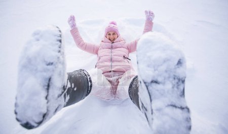 Foto de High angle view of happy woman lying on snow and moving her arms and legs Smiling woman lying on snow in winter holiday - Imagen libre de derechos