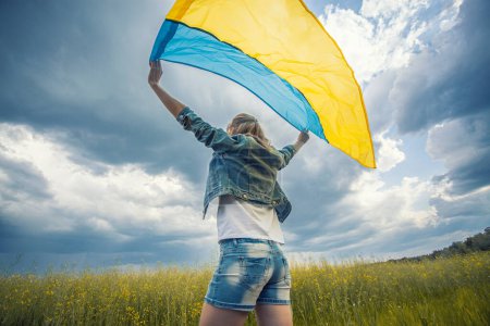 Foto de Mujer joven con bandera ucraniana en campo de colza. ondeando bandera nacional rezando por la paz. Chica feliz celebrando el Día de la Independencia. - Imagen libre de derechos