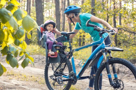 Foto de Madre con un bebé pequeño en bicicleta. Ciclismo familiar en el bosque de pinos de verano - Imagen libre de derechos