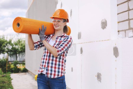 Foto de La trabajadora con rollos de fibra de vidrio reforzada. Aislamiento de la casa con tablero de poliespuma en la fachada - Imagen libre de derechos