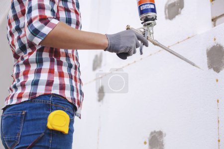 Photo for Insulation of the house with polyfoam. The woman worker foaming joints of polystyrene board on the facade. - Royalty Free Image